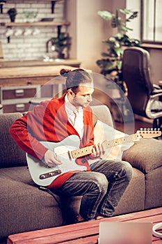 Bearded instrumentalist sitting on sofa and playing the guitar photo