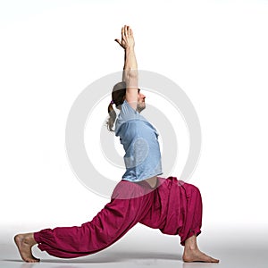 Bearded longhair man practicing yoga. Model doing Virabadrasana pose.