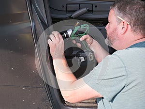 A bearded male mechanic works on a motorhome recreational vehicle with a power drill.