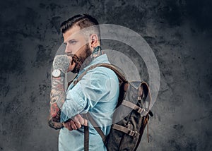 Bearded male with tattoos on his arms holds urban backpack.