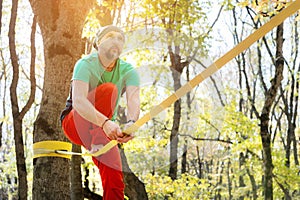 A bearded man in age balances while sitting on a taut slackline in the autumn forest. Outdoor Leisure