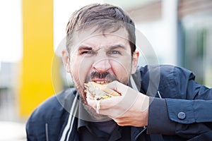 Bearded man with an appetite eating a hamburger on the street
