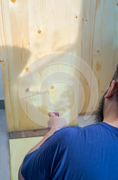 Bearded man applying clear coat paint on a wooden surface with roller brush. Painting wood wall and floor