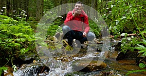 A bearded man with a backpack drinks water from a Mountain stream