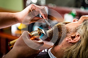 Bearded man in barbershop. Man visiting hairstylist in barbershop. Barber works with a beard clipper. Hipster client