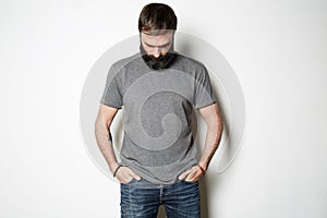 Bearded man in blank gray t-shirt, white wall on background
