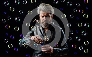 Bearded man blowing Soap bubbles. Handsome guy in leather jacket having fun playing with bubble.