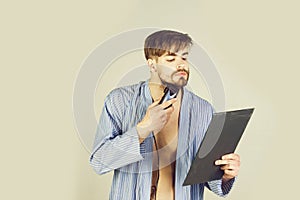 Bearded man in blue robe shaving beard with electric shaver