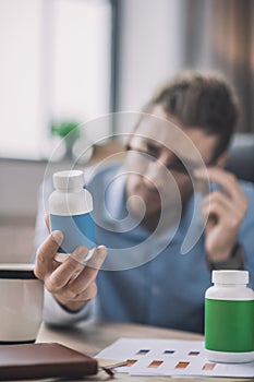 Bearded man in blue shirt looking at the botle with pills