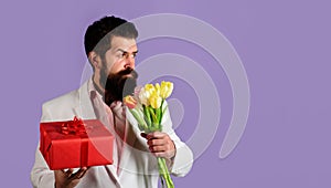 Bearded man with bouquet of flowers and gift box. Romantic man with bouquet of tulips. Businessman with present on