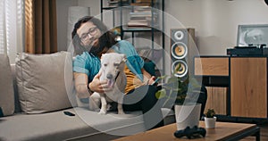 A bearded man browses the web on a smartphone in the company of dog. A contented young boy uses phone while sitting on