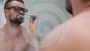 Bearded man brushing his teeth in a bathroom in the morning. Morning hygiene.