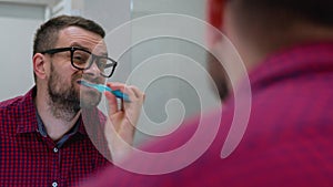 Bearded man brushing his teeth in a bathroom in the morning. Morning hygiene.