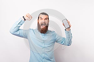Bearded man is celebrating victory while holding his phone.