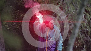 Bearded man in colorful jacket and round glasses swinging red burning signal flare and waiting to be found. Stock