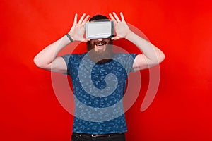 Bearded man is covering his eyes with screen of a tablet.