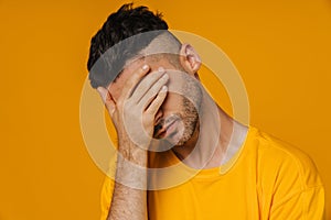 Bearded man covering his face with hand while standing isolated