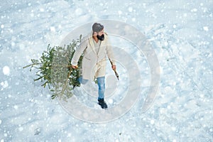 Bearded Man cutting Christmas tree. Happy father with Christmas tree on a snowy winter walk. Hipster woodsman with