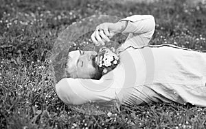 Bearded man with daisy flowers in beard lay on grassplot, grass background. Man with beard on calm face sniffs dandelion photo