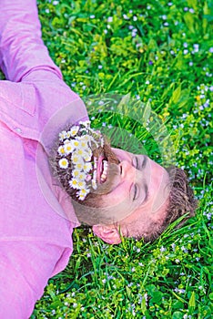 Bearded man with daisy flowers lay on grassplot, grass background. Hipster with bouquet of daisies in beard relaxing