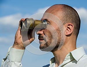 Bearded man detective looks through binoculars in the distance a