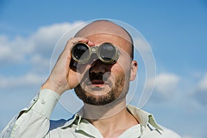 Bearded man detective looks through binoculars in the distance a