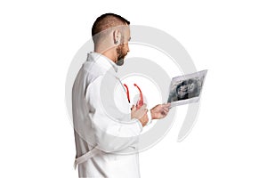 Bearded man, doctor in white med gown looking at x-ray scan checking health condition against white background