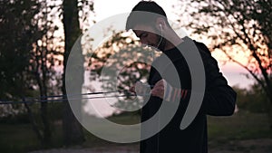 Bearded man doing arm exercises outdoors using resistance band outdoors in nature. Morning dusk, trees silhouettes on