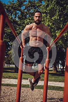 Bearded man doing dips and looking in to the camera