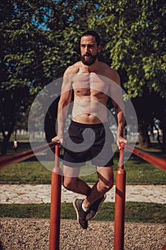 Bearded man doing dips on the outdoor bars