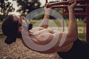 Bearded man doing romanian pull up in the outdoor gym