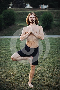 Bearded man doing yoga in the green park.