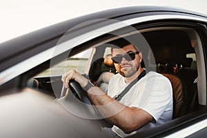 Bearded man driver in sunglasses sitting in his car and looking at camera