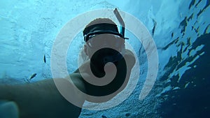 Bearded man engaged in scuba diving floats to the surface of the sea and shows a victory sign