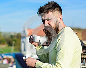 Bearded man with espresso mug, drinks coffee. Man with beard and mustache on strict face drinks coffee, urban background