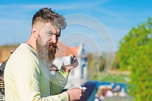 Bearded man with espresso mug, drinks coffee. Man with beard and mustache on strict face drinks coffee, urban background