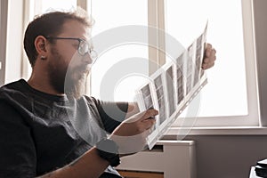 Bearded man examining film negatives by window light