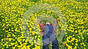 Bearded man in field of yellow dandelions lies resting in a field of dandelions