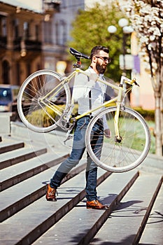 Bearded man with fix bicycle. View of confident young bearded man carrying his bicycle on shoulder and looking away while walking