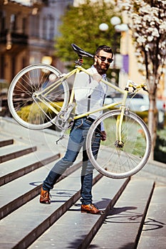 Bearded man with fix bicycle. View of confident young bearded man carrying his bicycle on shoulder and looking away while walking