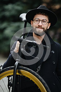 Bearded man with a fixie bicycle. Low angle view of confident young bearded man carrying his bicycle on shoulder and looking at