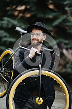Bearded man with a fixie bicycle. Low angle view of confident young bearded man carrying his bicycle on shoulder and looking at