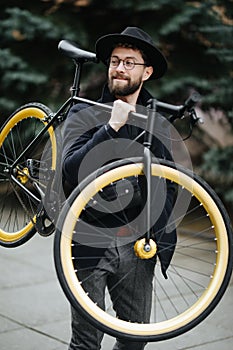 Bearded man with fixie bicycle. Low angle view of confident young bearded man carrying his bicycle on shoulder and looking away