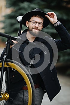 Bearded man with fixie bicycle. Low angle view of confident young bearded man carrying his bicycle on shoulder and looking away