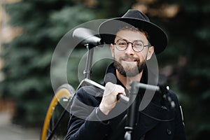 Bearded man with fixie bicycle. Low angle view of confident young bearded man carrying his bicycle on shoulder and looking away