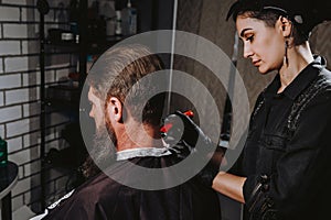 Bearded man getting haircut by hairdresser with dangerous razor at barbershop