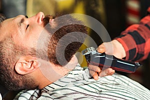 Bearded man is getting shaved by hairdresser at the barbershop. Beard care, perfect beard. Getting perfect shape