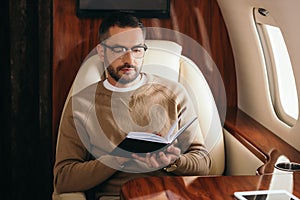 Bearded man in glasses looking at notebook in private jet