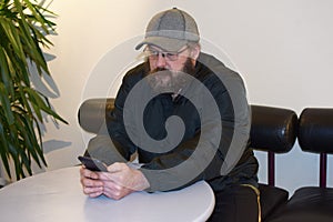 Bearded  man with glasses sits at a table in a public place