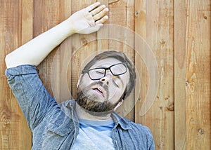 Bearded man in glasses was tired, lay down to rest on the wooden floor and fell asleep with his mouth open, in a funny pose,